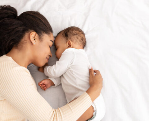 African Mother Hugging Sleeping Baby Lying In Bed Indoor, High Angle