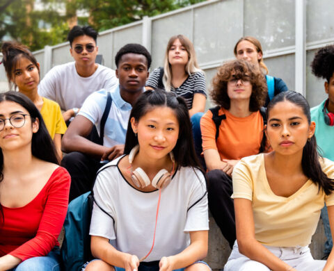 Group Of Multiracial Teen High School Students Looking At Camera Sit On Stairs Outdoors.